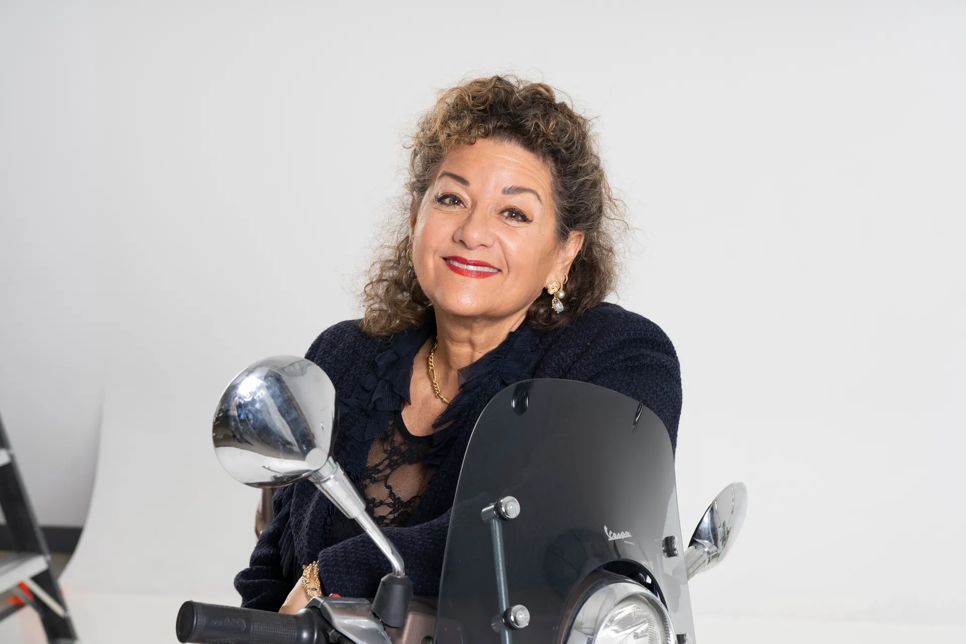 Sharon Azrieli derrière le pare-brise d'une Vespa, portrait rapproché en studio
